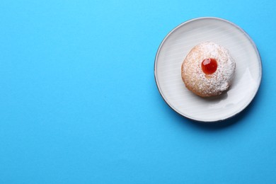 Photo of Hanukkah donut with jelly and powdered sugar on turquoise background, top view. Space for text