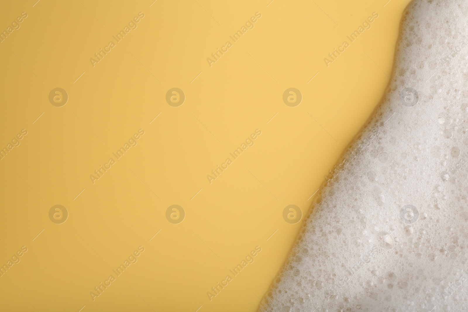 Photo of White fluffy foam on yellow background, top view. Space for text