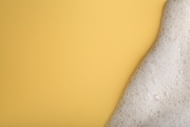 Photo of White fluffy foam on yellow background, top view. Space for text