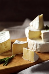 Wooden board with delicious cheeses on table