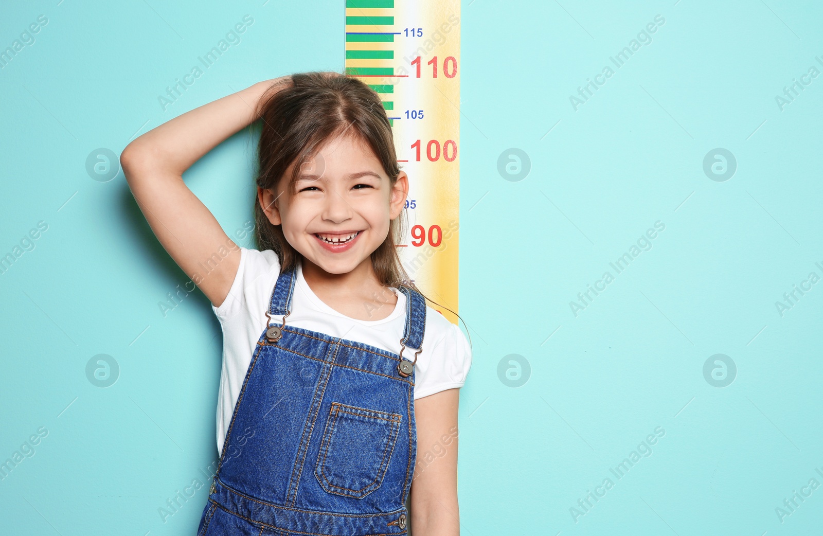 Photo of Little girl measuring her height on color background