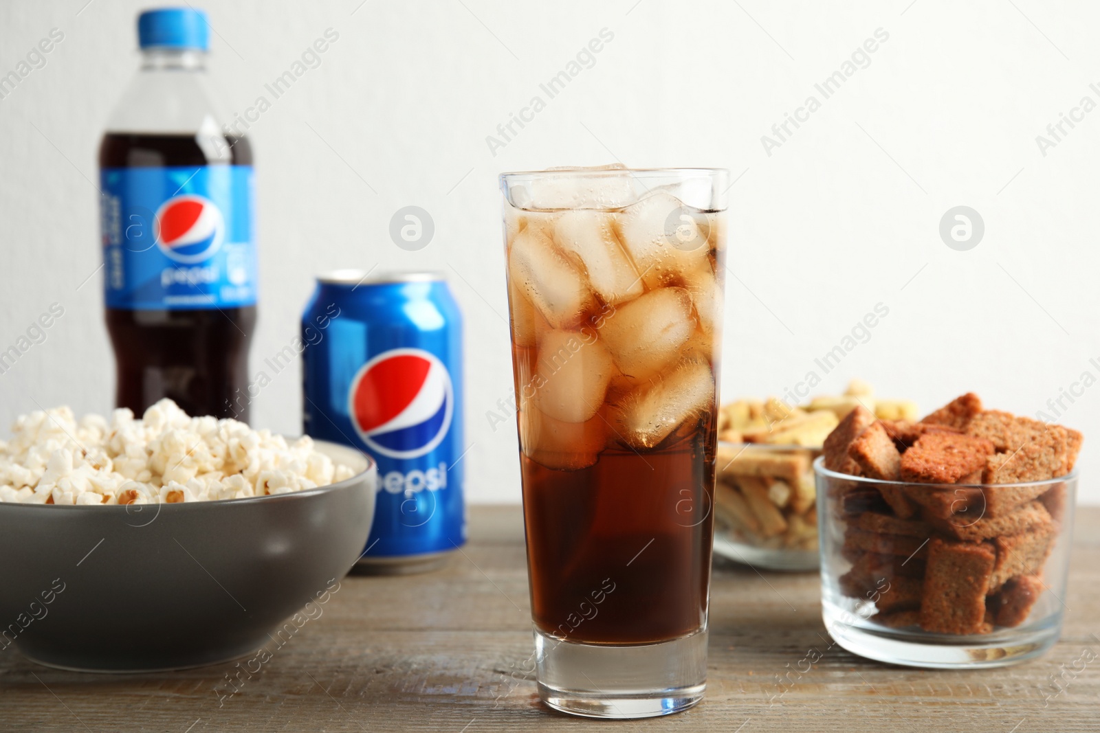 Photo of MYKOLAIV, UKRAINE - FEBRUARY 15, 2021: Glass of Pepsi and snacks on wooden table