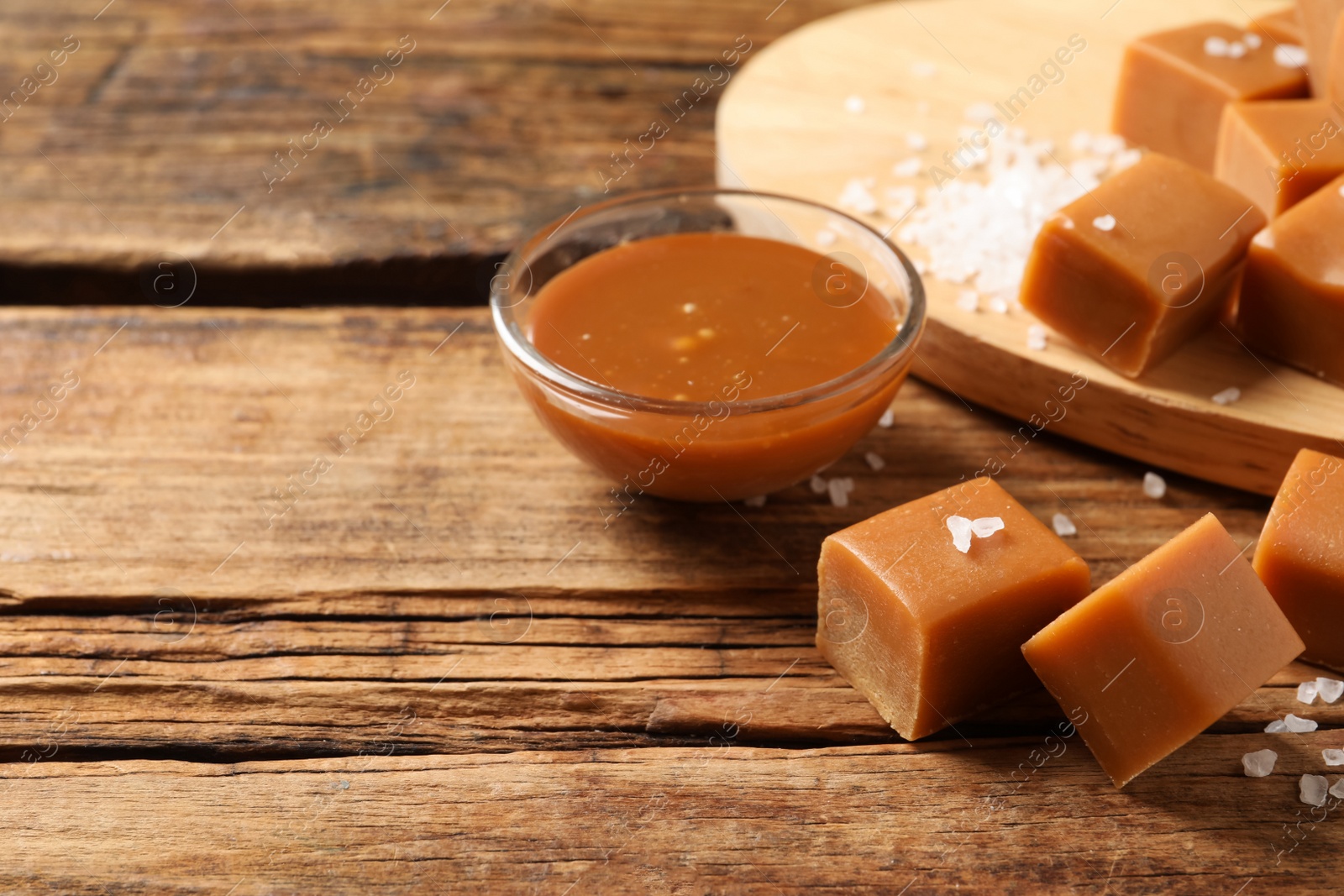 Photo of Yummy salted caramel in bowl and candies on wooden table, space for text