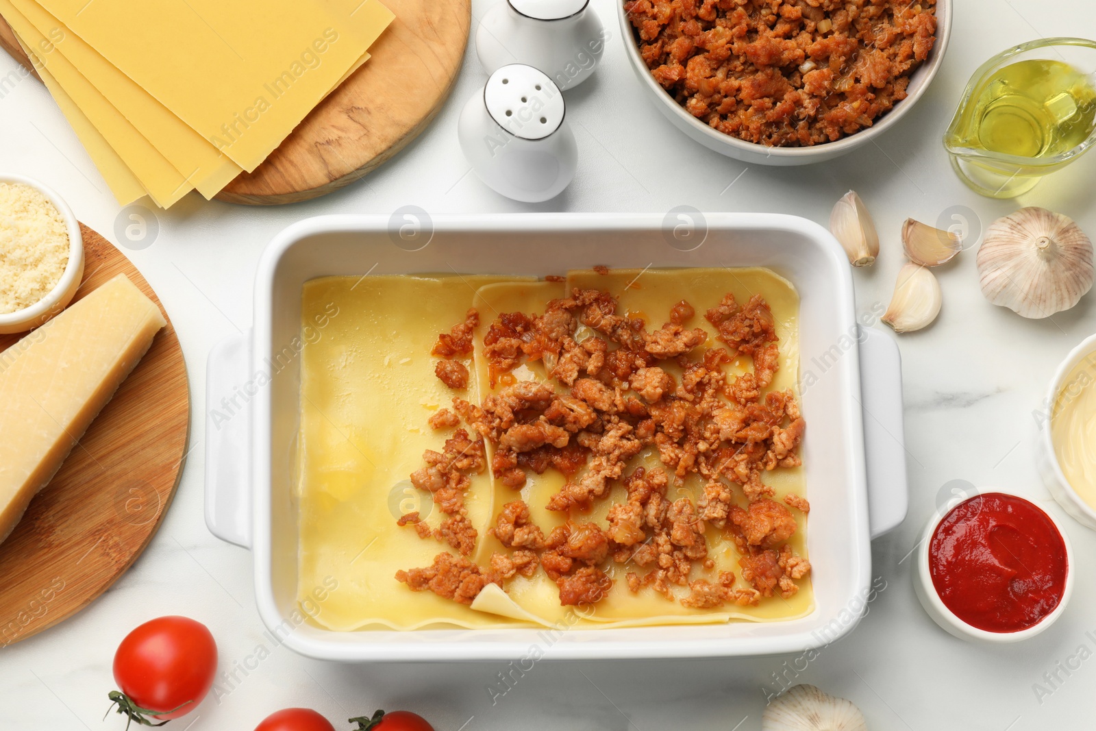 Photo of Cooking lasagna. Pasta sheets, minced meat in baking tray and products on white table, flat lay