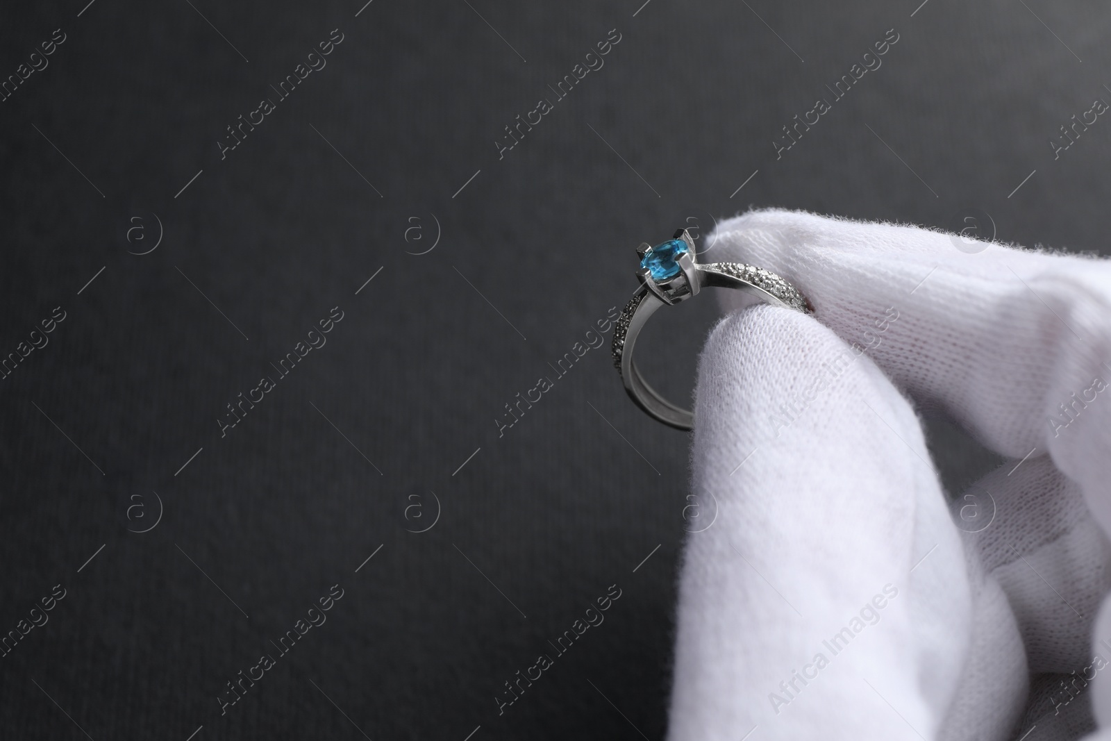Photo of Jeweler holding topaz ring on dark grey background, closeup. Space for text
