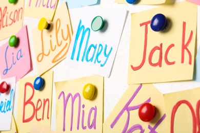 Photo of Colorful paper sheets with written different baby names on white background, closeup