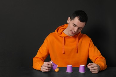 Photo of Shell game. Man showing ball under cup at black table