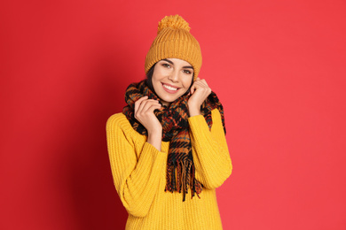 Young woman wearing warm sweater, scarf and hat on red background. Winter season