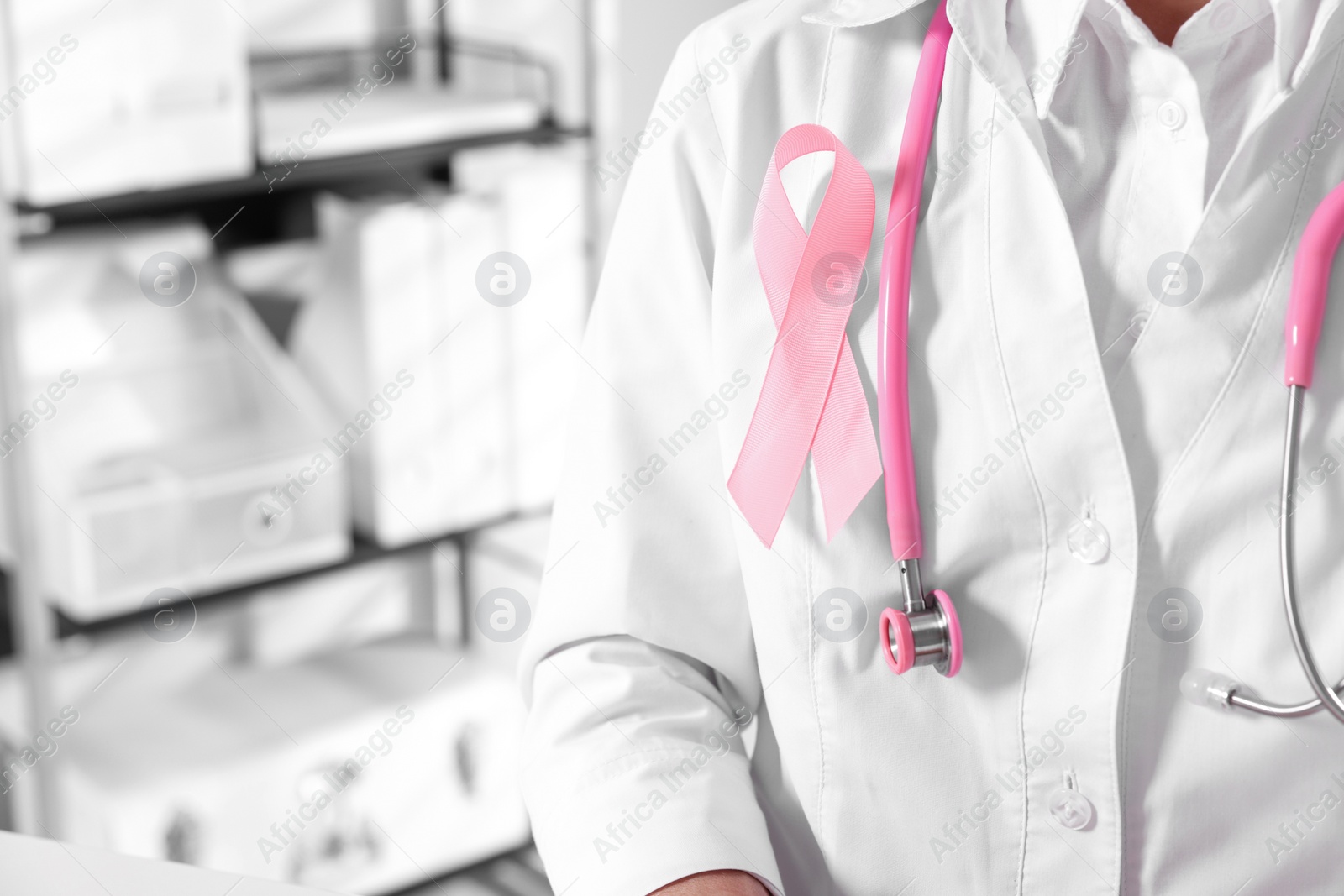Photo of Doctor with stethoscope and pink ribbon indoors, closeup and space for text. Breast cancer awareness