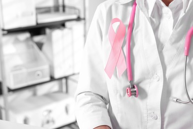 Doctor with stethoscope and pink ribbon indoors, closeup and space for text. Breast cancer awareness