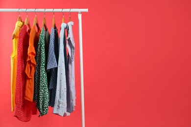 Photo of Bright clothes hanging on rack against red background, space for text. Rainbow colors