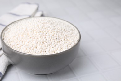 Photo of Tapioca pearls in bowl and towel on white tiled table, closeup