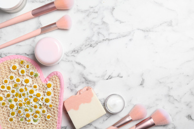 Flat lay composition with chamomile flowers and cosmetic products on white marble table, space for text