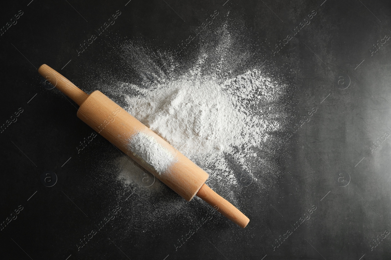 Photo of Scattered flour and rolling pin on black table, top view. Space for text