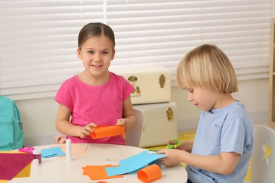 Cute children making paper toys at desk in room. Home workplace