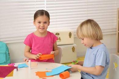 Photo of Cute children making paper toys at desk in room. Home workplace