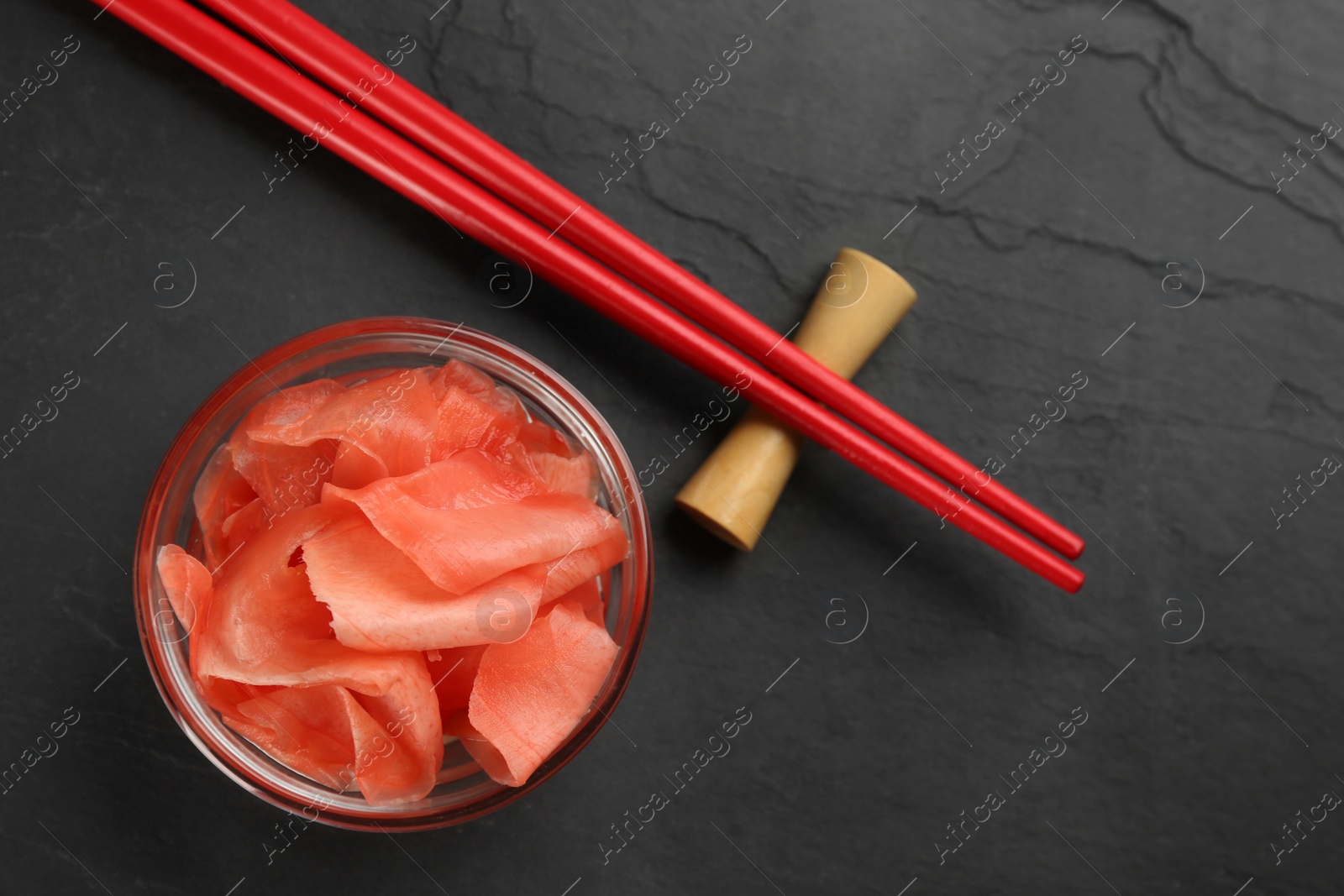 Photo of Pickled ginger in bowl and chopsticks on black table, flat lay