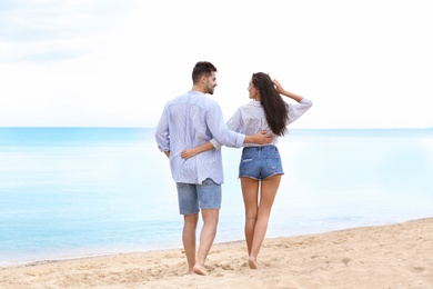 Happy young couple walking together on beach near sea