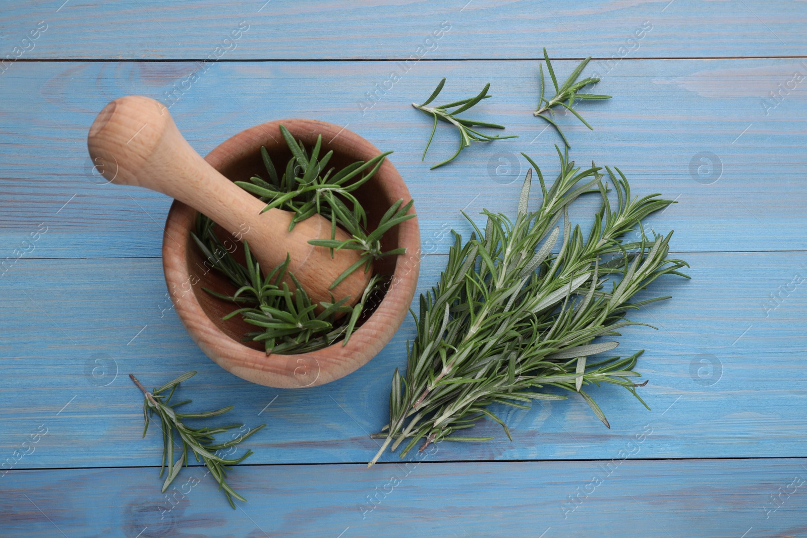 Photo of Sprigs of fresh rosemary and mortar on light blue wooden table, flat lay