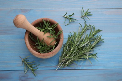 Photo of Sprigs of fresh rosemary and mortar on light blue wooden table, flat lay