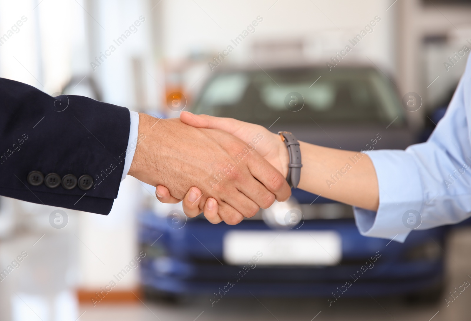 Photo of Young salesman shaking hands with client in car dealership