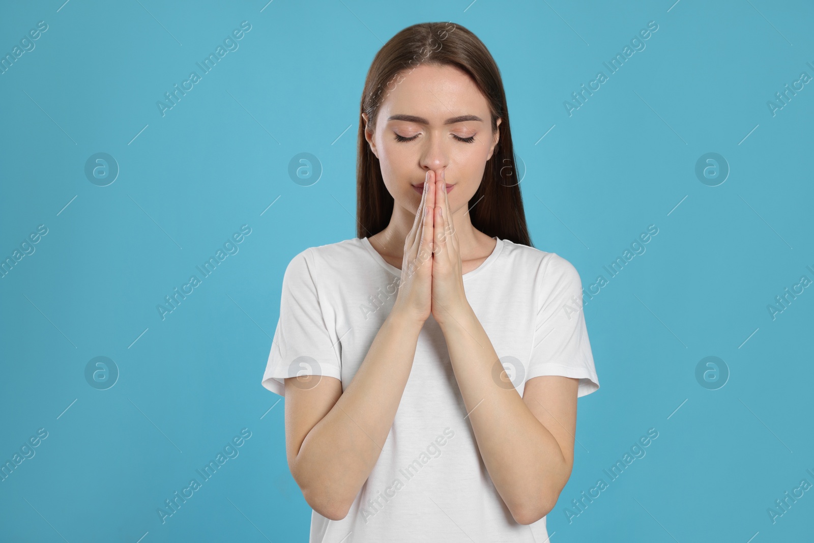 Photo of Woman with clasped hands praying on turquoise background