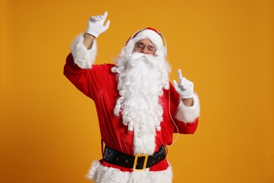 Photo of Merry Christmas. Santa Claus with headphones listening to music on orange background