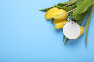 Photo of Bouquet of beautiful yellow tulips and blank card on light blue background, top view with space for text. Birthday celebration