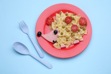 Photo of Creative serving for kids. Plate with cute hedgehog made of delicious pasta, sausages and tomatoes on light blue table, flat lay