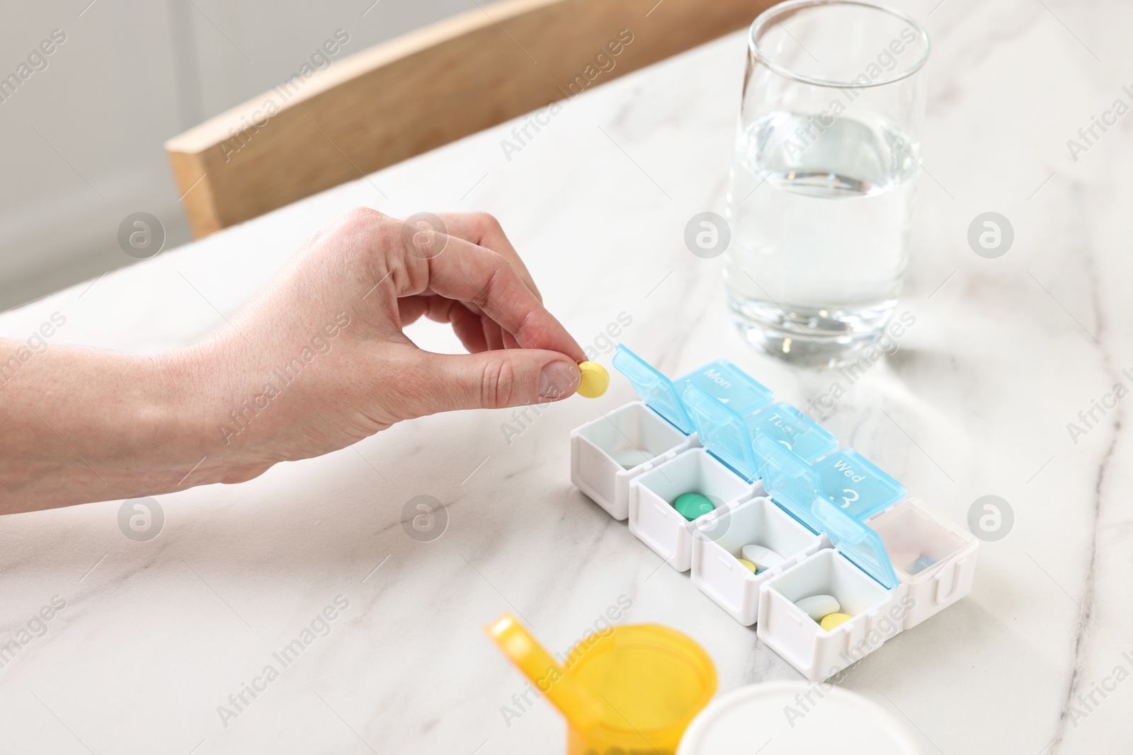 Photo of Woman with pills, organizer and glass of water at white marble table, closeup