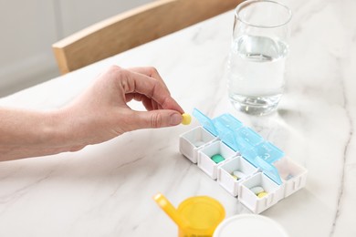 Photo of Woman with pills, organizer and glass of water at white marble table, closeup