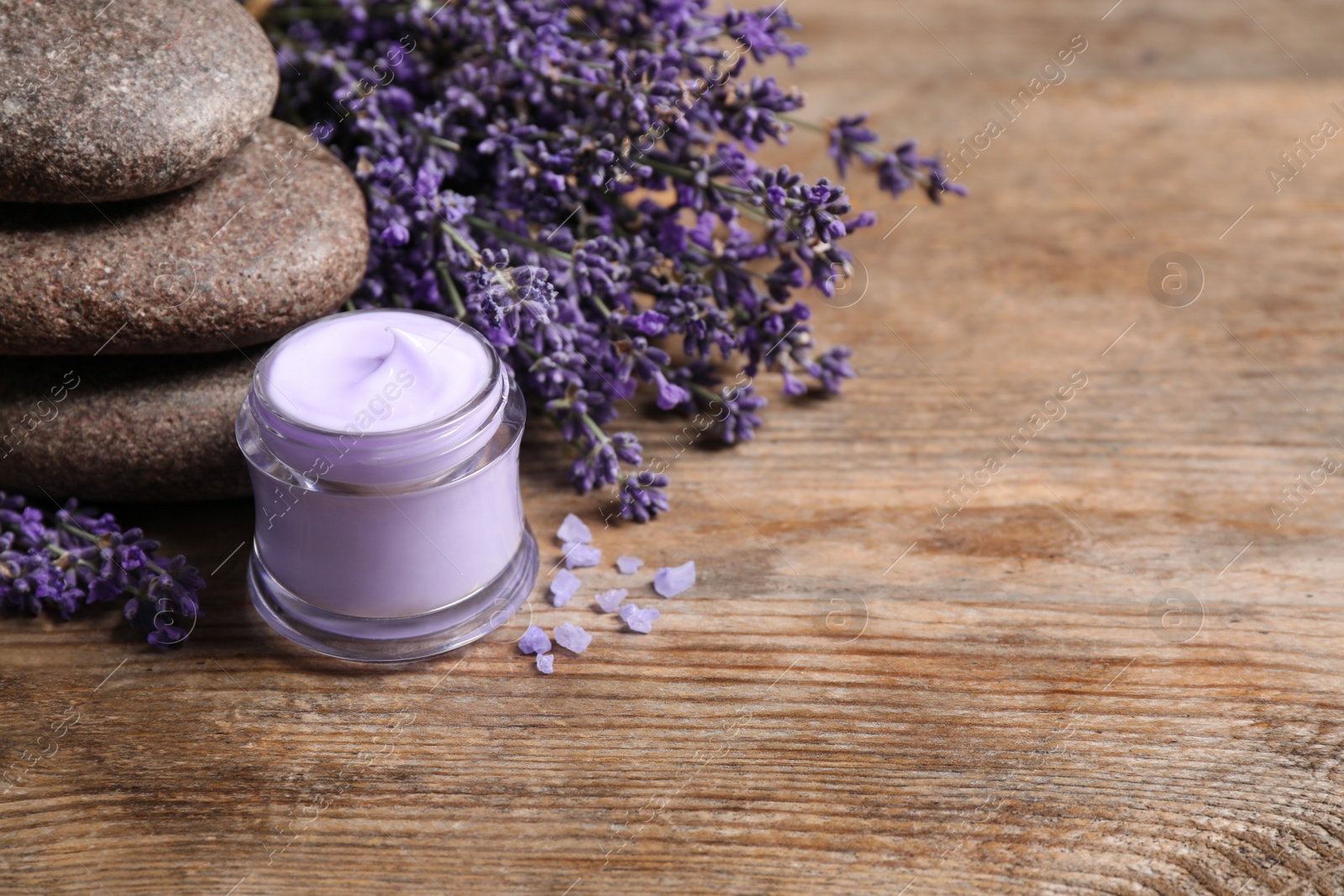 Photo of Stones, jar of cream and lavender flowers on wooden table. Space for text