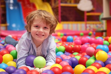 Happy little boy lying on colorful balls in ball pit, space for text