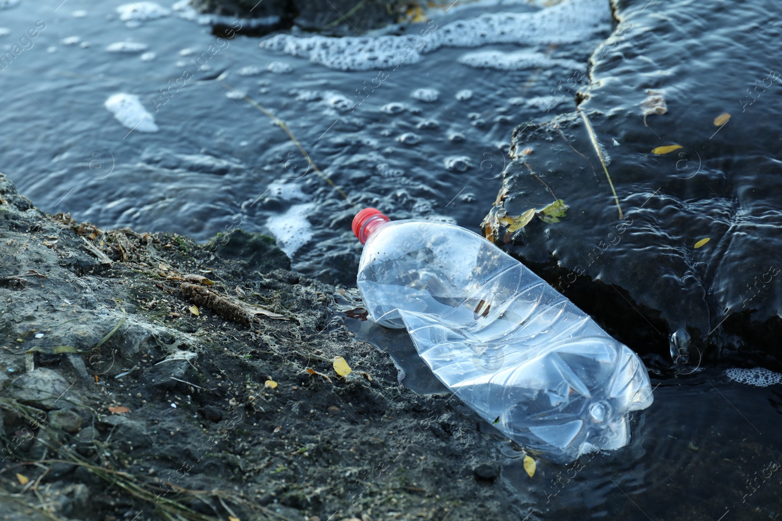 Photo of Used plastic bottle near water outdoors, space for text. Environment pollution