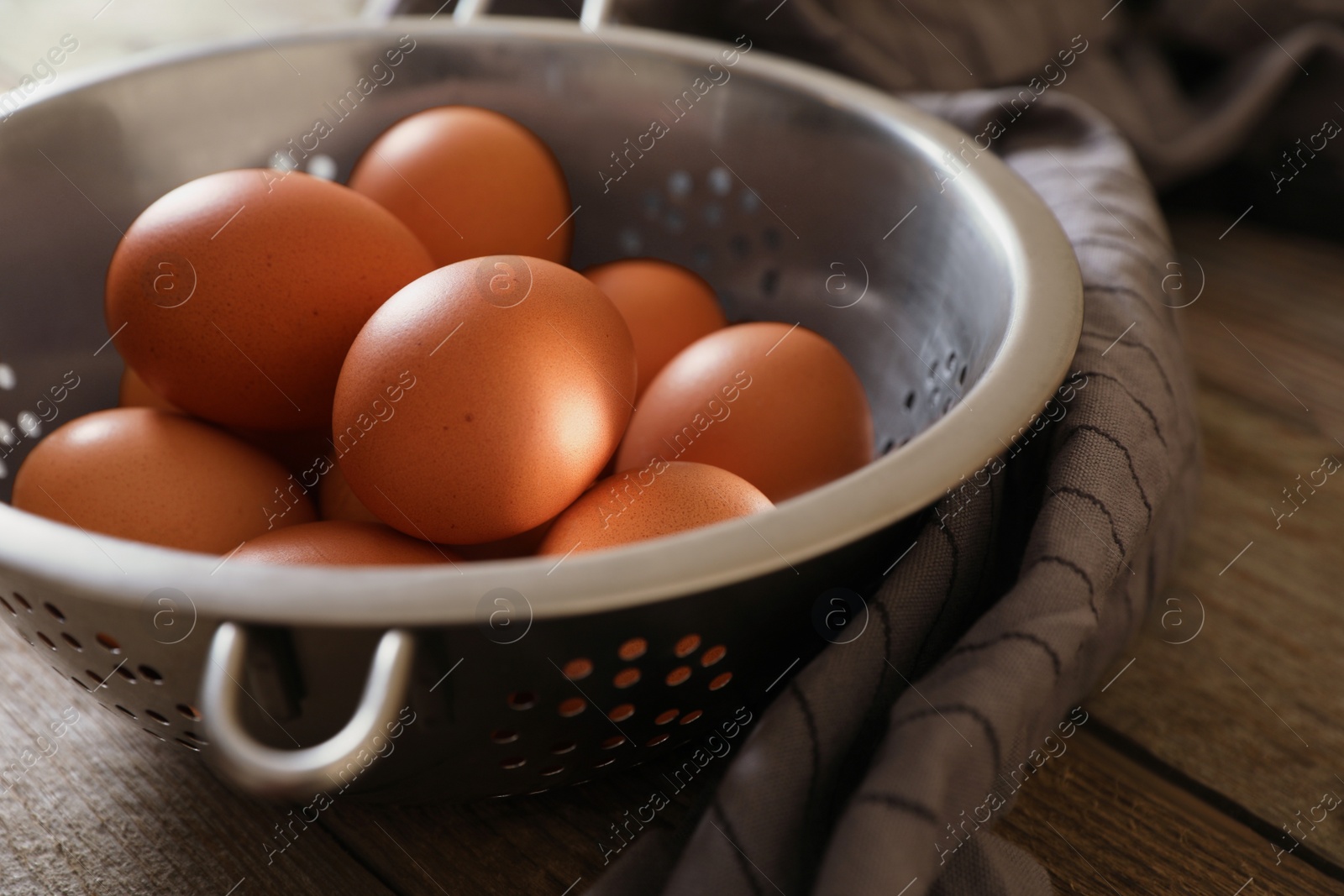 Photo of Chicken eggs in colander and napkin on wooden table