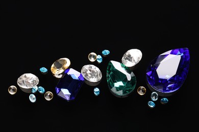 Different beautiful gemstones for jewelry on black background, flat lay