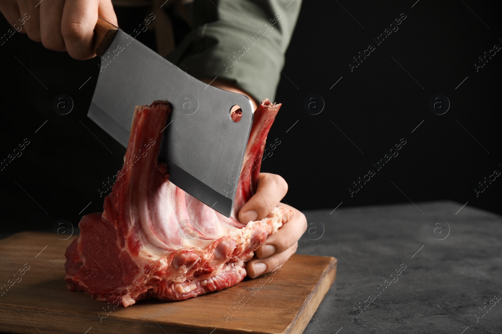 Photo of Man cutting raw ribs at grey table, closeup. Space for text