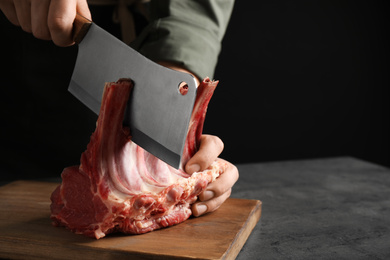 Photo of Man cutting raw ribs at grey table, closeup. Space for text