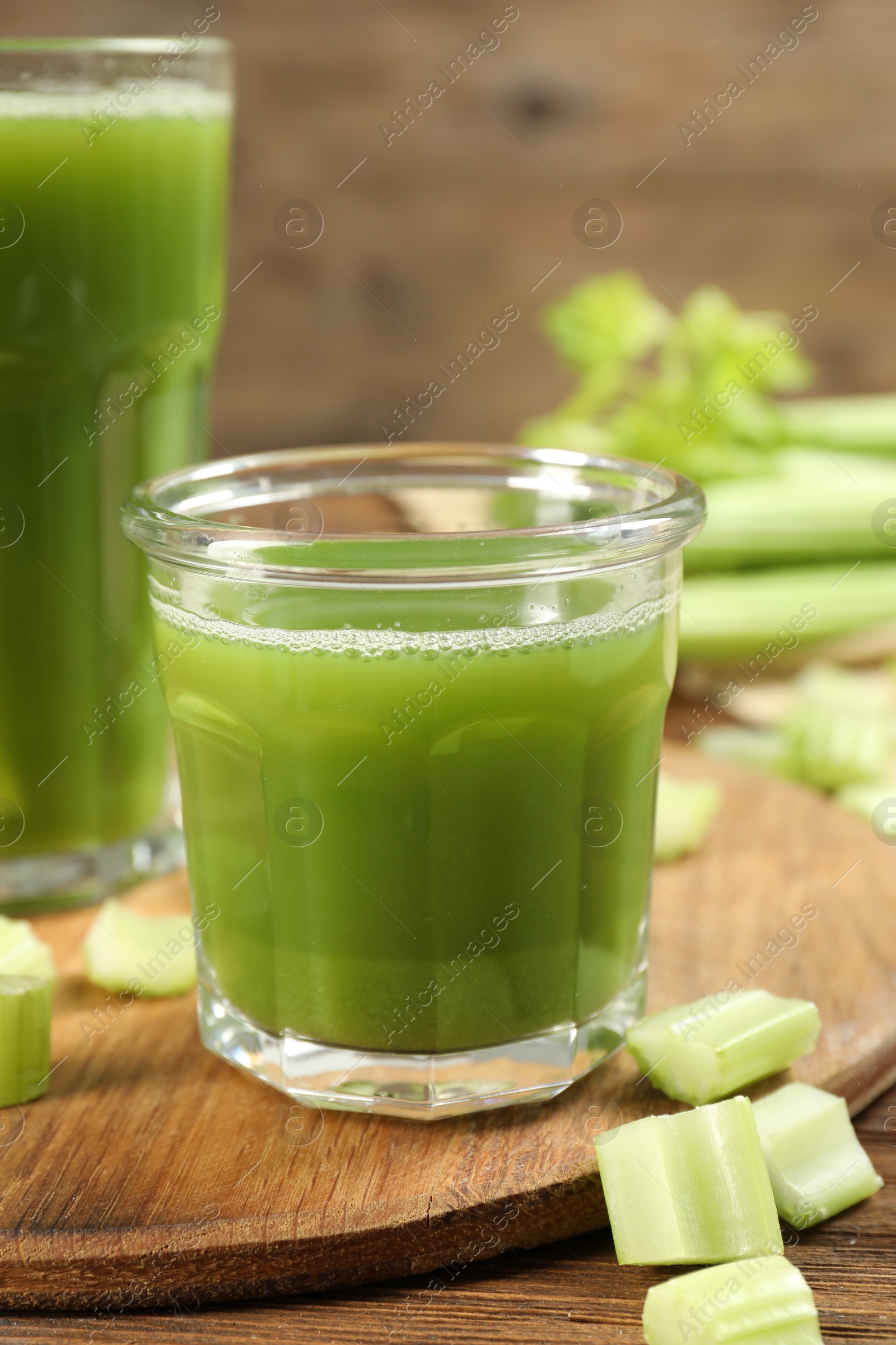 Photo of Glass of celery juice and fresh vegetable on wooden table, closeup