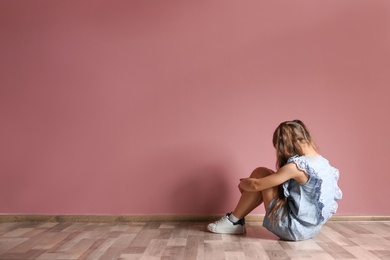 Little girl sitting on floor near color wall in empty room. Autism concept