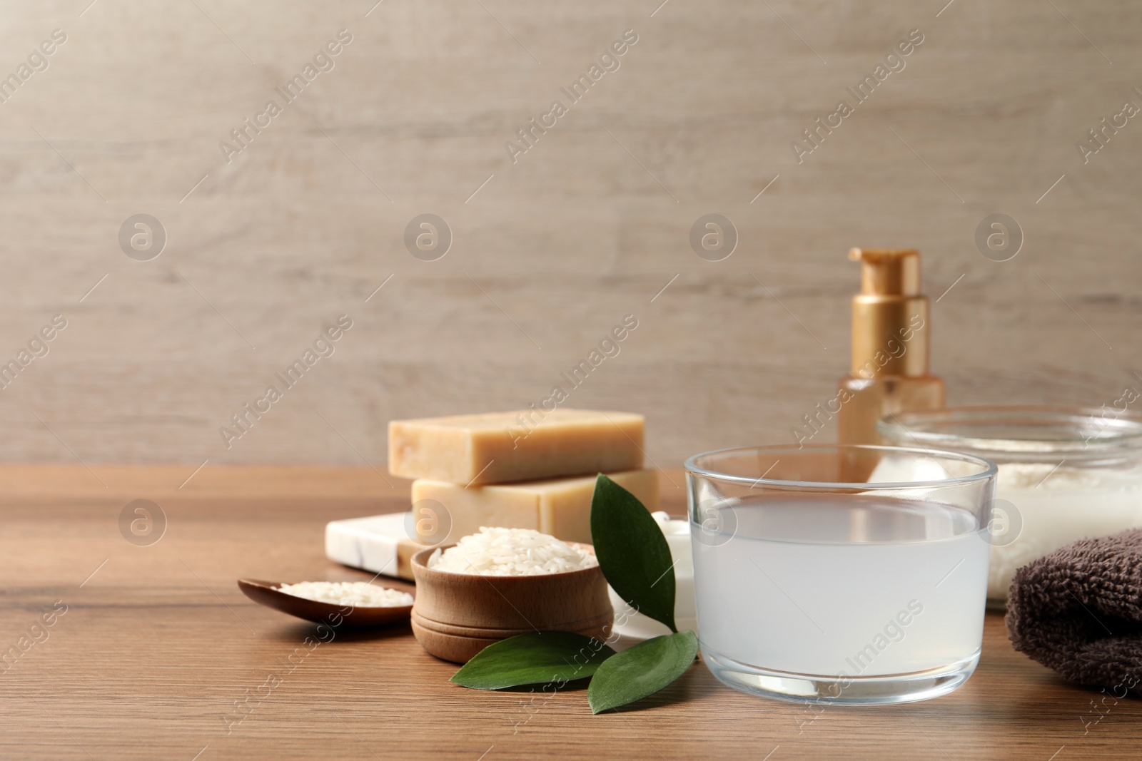 Photo of Homemade natural rice water and cosmetic products on wooden table. Space for text