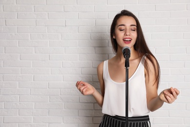 Photo of Young woman wearing casual clothes singing in microphone near brick wall. Space for text