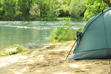 Modern camping tent on riverbank in wilderness. Space for text