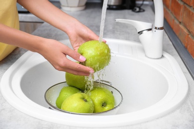 Woman washing fresh apples in kitchen sink, closeup