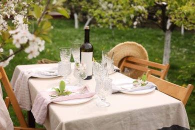 Photo of Stylish table setting with beautiful spring flowers, wine, plates and glasses in garden