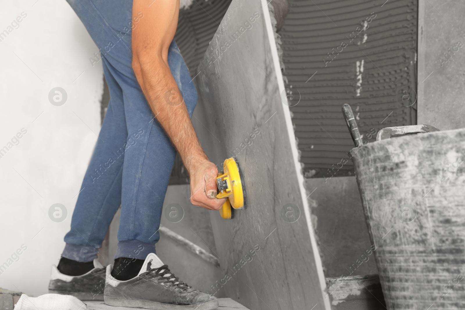 Photo of Worker installing wall tile with vacuum holder indoors, closeup