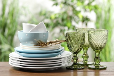 Photo of Beautiful ceramic dishware, glasses and cutlery on wooden table outdoors