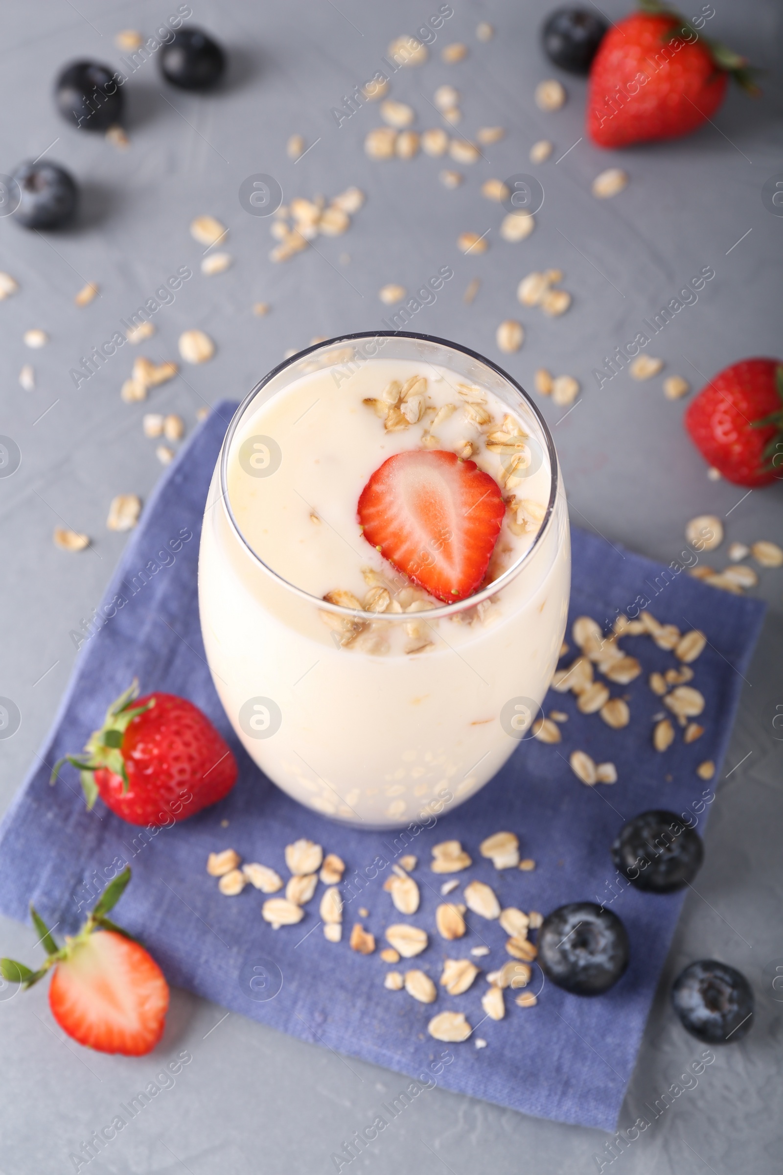 Photo of Tasty yogurt in glass, oats and berries on grey table