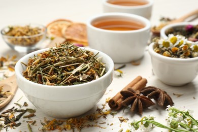 Bowl of dry aromatic tea on white wooden table, space for text