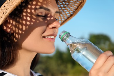 Photo of Happy woman in straw hat drinking water outdoors on hot summer day, closeup. Refreshing drink